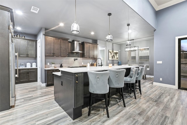 kitchen featuring light hardwood / wood-style flooring, dark brown cabinets, pendant lighting, a large island, and wall chimney range hood