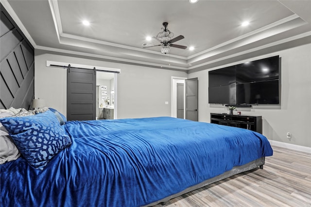 bedroom with ornamental molding, a barn door, light wood-type flooring, and a tray ceiling