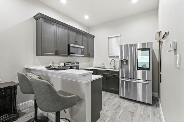 kitchen featuring a kitchen bar, sink, kitchen peninsula, stainless steel appliances, and light hardwood / wood-style floors