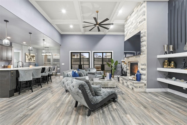 living room with coffered ceiling, beamed ceiling, ceiling fan, a fireplace, and light hardwood / wood-style floors