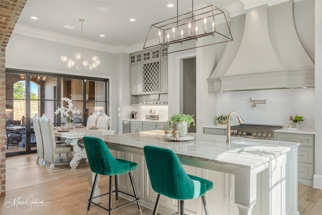 kitchen featuring custom exhaust hood, light stone counters, light wood-type flooring, pendant lighting, and a large island