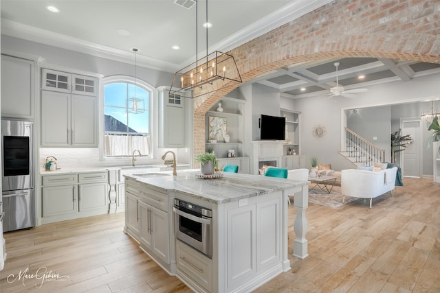 kitchen featuring sink, light hardwood / wood-style flooring, a kitchen island with sink, stainless steel appliances, and decorative light fixtures