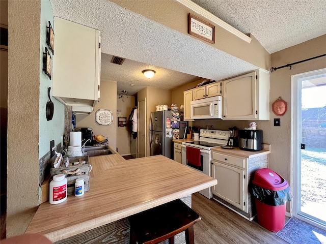 kitchen featuring wood-type flooring, sink, white appliances, kitchen peninsula, and a textured ceiling