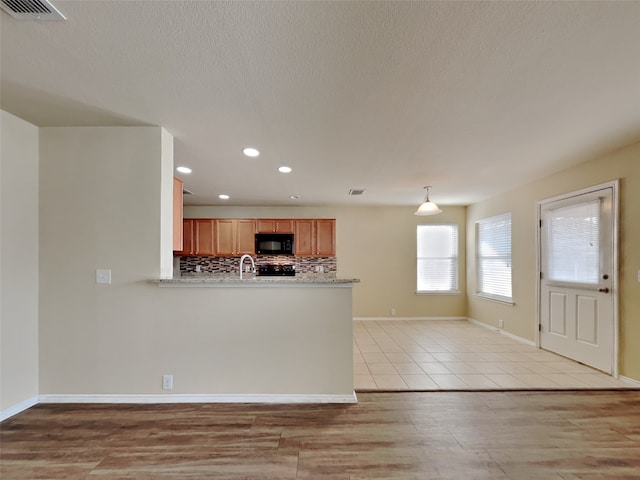 kitchen with tasteful backsplash, a textured ceiling, decorative light fixtures, kitchen peninsula, and light wood-type flooring