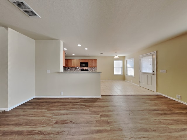 unfurnished living room with sink, a textured ceiling, and light hardwood / wood-style flooring