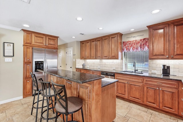 kitchen featuring sink, appliances with stainless steel finishes, a kitchen breakfast bar, a center island, and dark stone counters