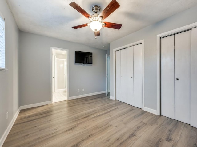 unfurnished bedroom with multiple closets, ensuite bathroom, ceiling fan, and light hardwood / wood-style floors