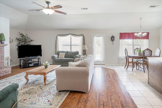 living room featuring lofted ceiling, ceiling fan with notable chandelier, and light wood-type flooring