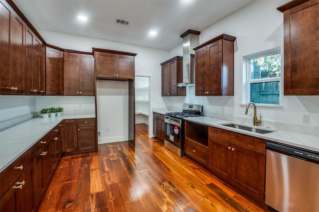 kitchen with sink, wall chimney range hood, dark wood-type flooring, appliances with stainless steel finishes, and light stone countertops