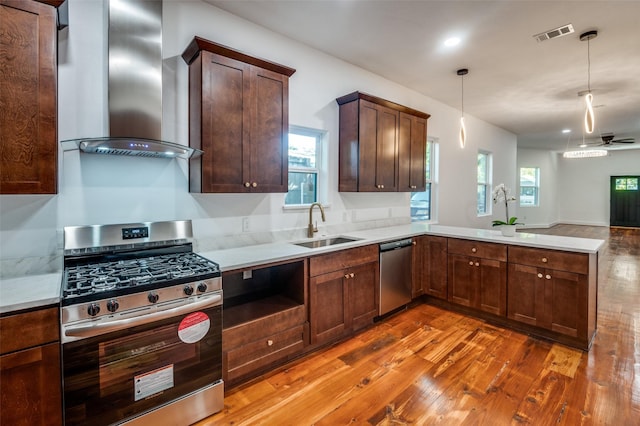 kitchen featuring wall chimney exhaust hood, sink, decorative light fixtures, kitchen peninsula, and stainless steel appliances