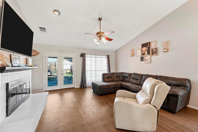 living room with vaulted ceiling, a fireplace, hardwood / wood-style flooring, ceiling fan, and french doors