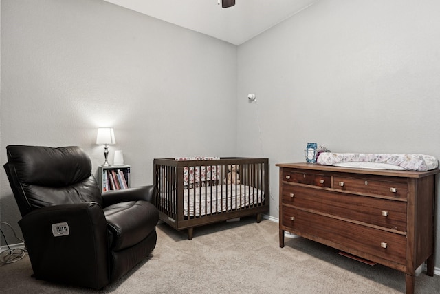 bedroom featuring a crib, light colored carpet, and ceiling fan