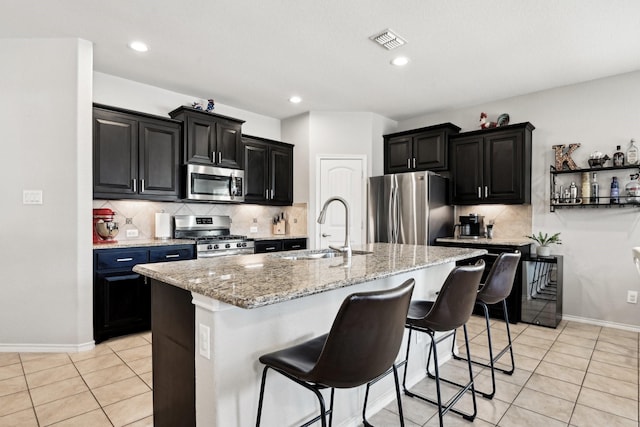 kitchen featuring sink, light tile patterned floors, a breakfast bar, appliances with stainless steel finishes, and an island with sink