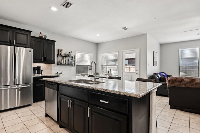 kitchen with sink, light tile patterned floors, appliances with stainless steel finishes, a kitchen island with sink, and decorative backsplash