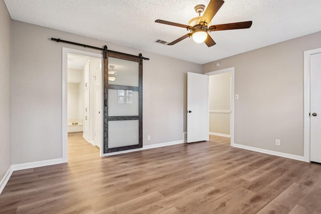 201 Trailwood Dr, Euless, TX 76039 - unfurnished bedroom with wood-type flooring, a barn door, a textured ceiling, and ensuite bathroom