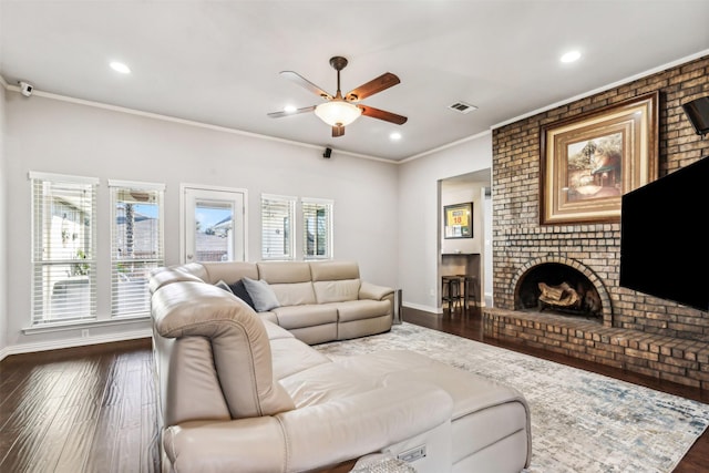 living room featuring ceiling fan, ornamental molding, dark hardwood / wood-style flooring, and a brick fireplace