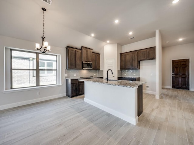 kitchen featuring backsplash, hanging light fixtures, light stone countertops, a center island with sink, and light hardwood / wood-style flooring