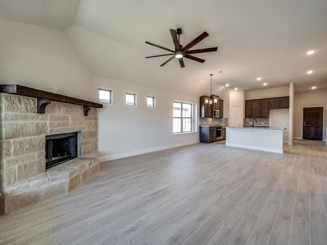 unfurnished living room with vaulted ceiling, a stone fireplace, sink, ceiling fan, and light wood-type flooring