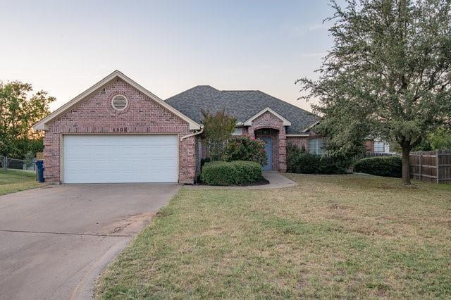 single story home with brick siding, a lawn, an attached garage, fence, and driveway