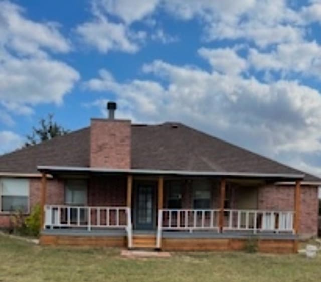 rear view of property with a chimney, a porch, and a yard