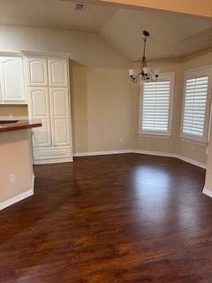 unfurnished dining area featuring an inviting chandelier, dark wood-type flooring, and vaulted ceiling