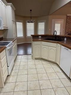 kitchen with white appliances, light tile patterned floors, dark countertops, white cabinetry, and a sink