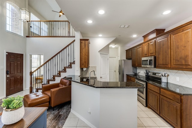 kitchen featuring light tile patterned floors, appliances with stainless steel finishes, kitchen peninsula, decorative backsplash, and dark stone counters