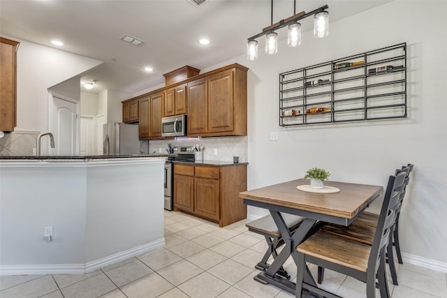 kitchen with dark stone countertops, decorative backsplash, hanging light fixtures, light tile patterned floors, and stainless steel appliances