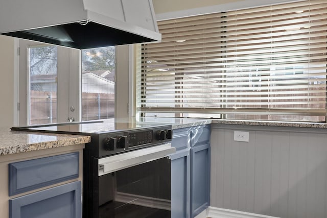 kitchen featuring blue cabinets, light stone countertops, electric range, and range hood