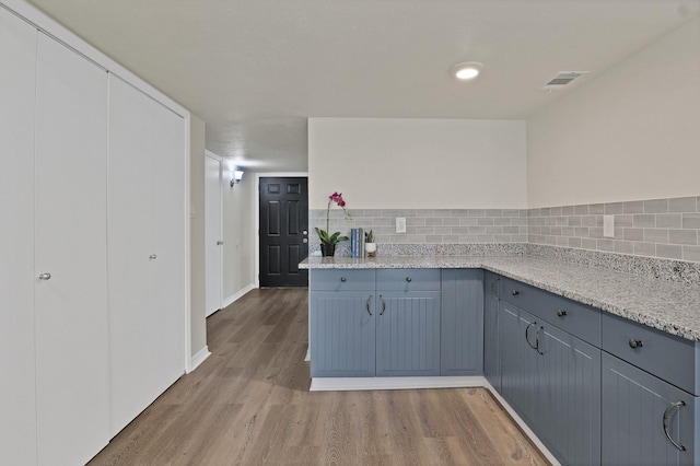 kitchen with hardwood / wood-style flooring, light stone counters, and tasteful backsplash