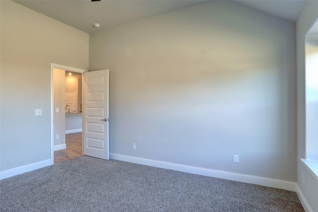 carpeted empty room featuring lofted ceiling and baseboards