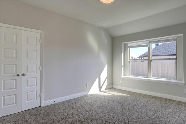 empty room featuring lofted ceiling, carpet, and baseboards