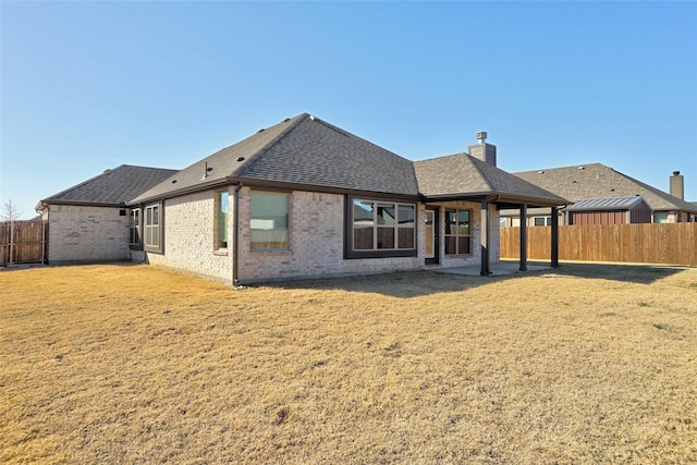 back of property featuring brick siding, a yard, a patio, roof with shingles, and a fenced backyard