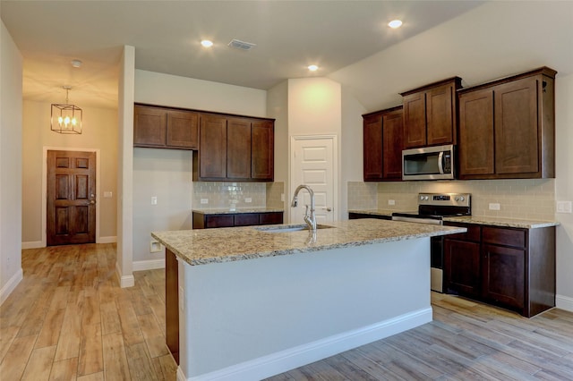 kitchen with sink, a center island with sink, light wood-type flooring, stainless steel appliances, and light stone countertops