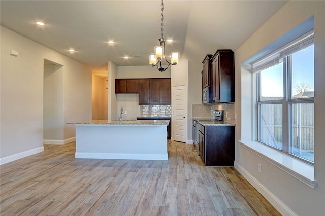 kitchen featuring appliances with stainless steel finishes, light wood-type flooring, light stone countertops, and tasteful backsplash