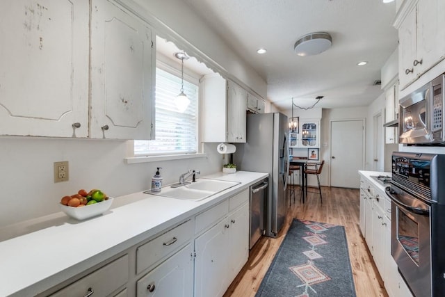 kitchen featuring sink, white cabinetry, decorative light fixtures, appliances with stainless steel finishes, and light hardwood / wood-style floors