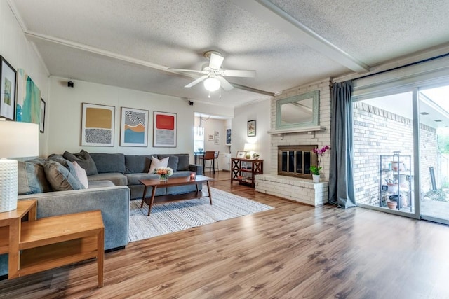 living room featuring a textured ceiling, ornamental molding, hardwood / wood-style flooring, ceiling fan, and a fireplace