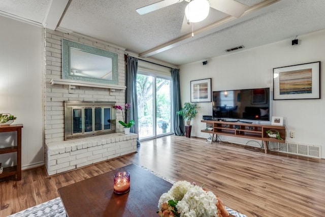 living room featuring hardwood / wood-style floors, a fireplace, beamed ceiling, ceiling fan, and a textured ceiling