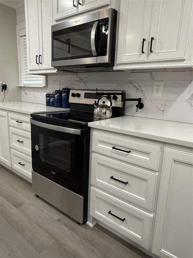 kitchen with white cabinetry, stainless steel appliances, decorative backsplash, and light hardwood / wood-style flooring