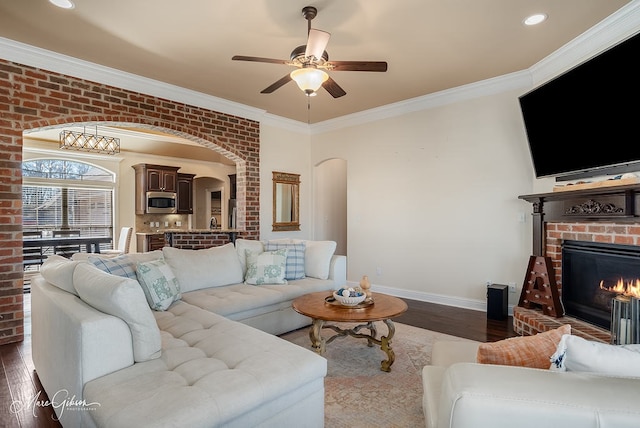 living room featuring ceiling fan, a fireplace, ornamental molding, and dark hardwood / wood-style floors