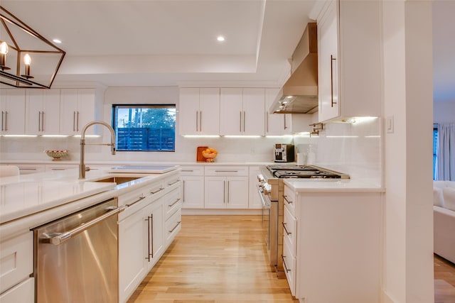 kitchen featuring wall chimney exhaust hood, sink, white cabinetry, decorative light fixtures, and stainless steel appliances