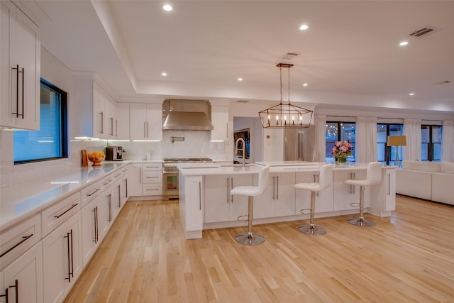 kitchen featuring white cabinetry, wall chimney exhaust hood, hanging light fixtures, and high end stove