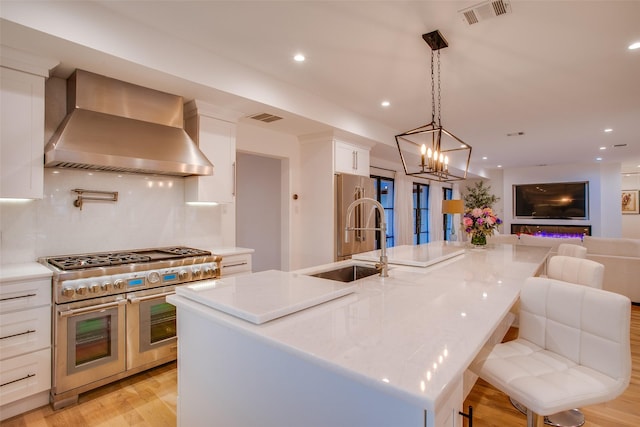 kitchen with a spacious island, wall chimney exhaust hood, a breakfast bar, high end appliances, and white cabinets