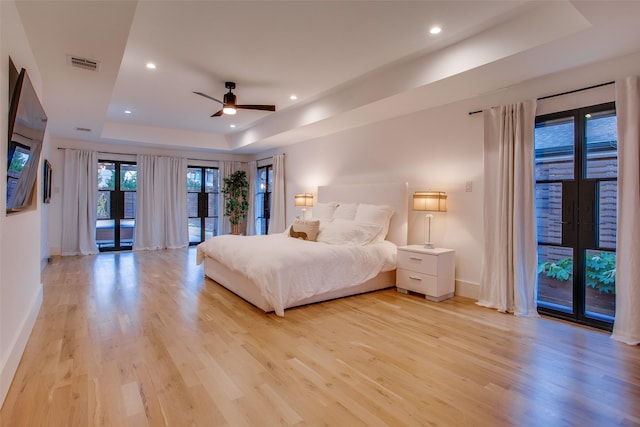 bedroom featuring a raised ceiling, access to exterior, light wood-type flooring, and french doors