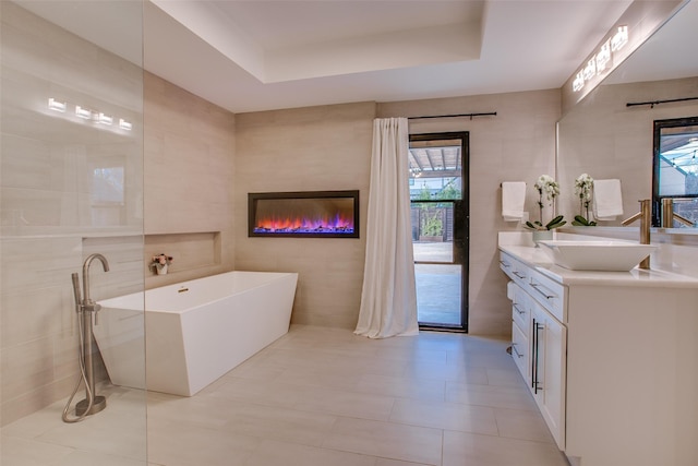 bathroom featuring tile patterned floors, tile walls, vanity, a tray ceiling, and a washtub