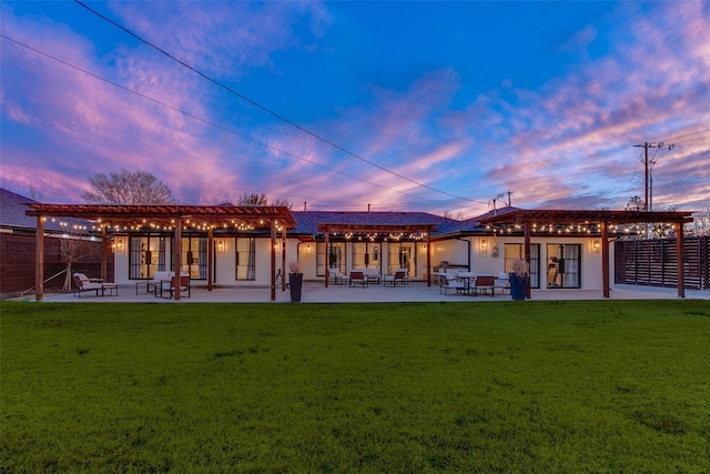 back house at dusk with a yard, a pergola, and a patio area