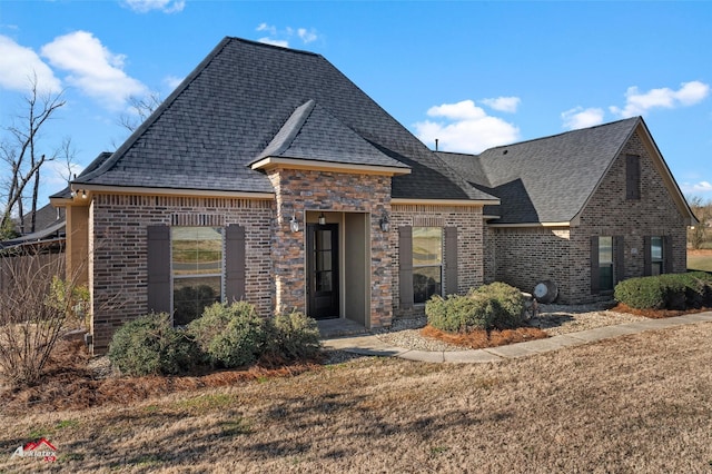 view of front of home with a shingled roof, brick siding, and a front yard