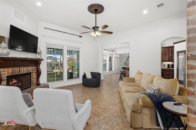 tiled living room with a brick fireplace, crown molding, and ceiling fan with notable chandelier