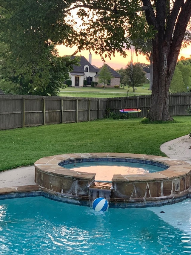 pool at dusk with pool water feature, an in ground hot tub, and a lawn