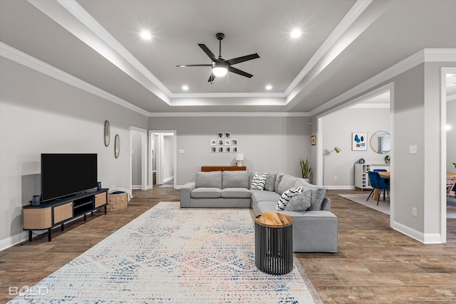 living room featuring a raised ceiling, ornamental molding, hardwood / wood-style flooring, and ceiling fan